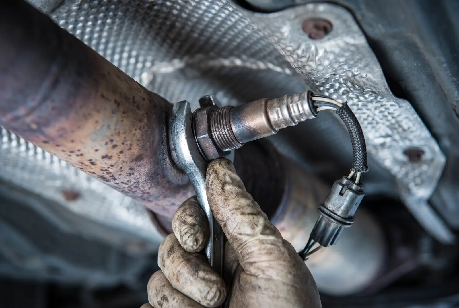 AI illustration: a downstream oxygen sensor threaded into the weathered exhaust pipe under a 2000s compact car